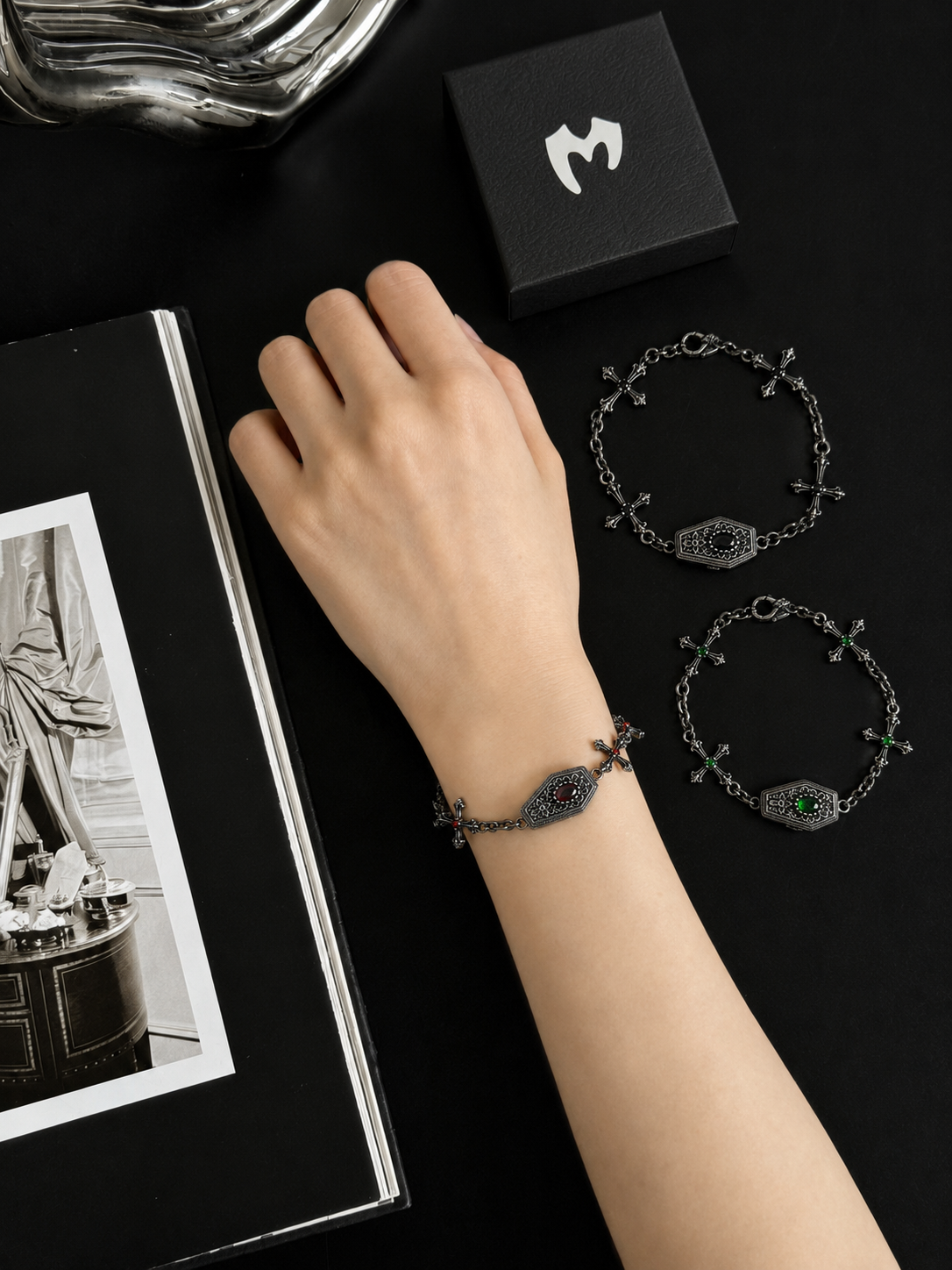Red gothic coffin cross bracelet worn on the wrist beside black and green variants